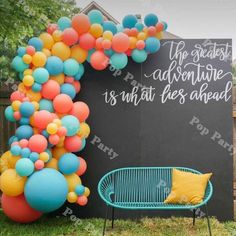 an arch made out of balloons is next to a blue bench with a yellow pillow on it