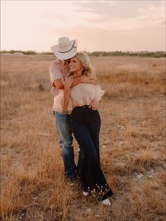 a man and woman hugging in the middle of an open field with tall dry grass