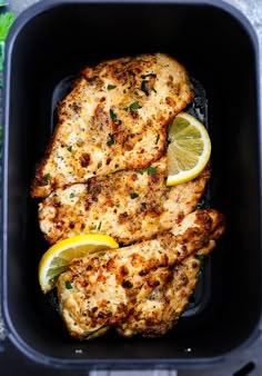 two pieces of chicken in a black container with lemons and parsley