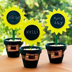 three small potted plants with fake sunflowers in them and writing on the stems