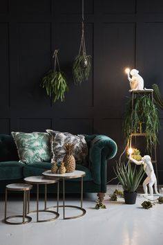 a living room filled with green furniture and potted plants on top of tables in front of a black wall