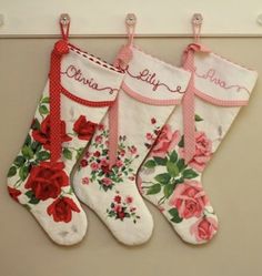 three christmas stockings hanging on a wall with roses and ribbons attached to the stocking