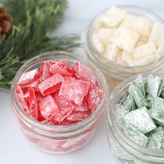 three glass bowls filled with different colored candies next to pine cones and evergreen branches