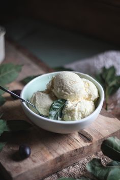 a bowl filled with ice cream sitting on top of a wooden cutting board next to leaves