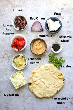 the ingredients to make an artichoke pizza laid out on a white table top