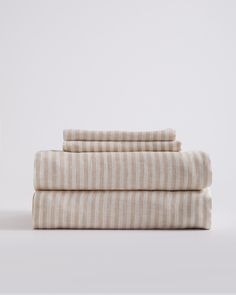 three sheets folded on top of each other in beige and white striped linens, against a light gray background