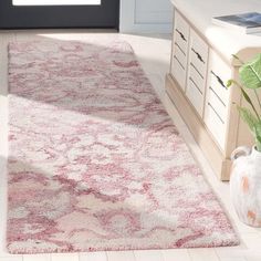 a white and pink rug in a living room next to a dresser with vases on it