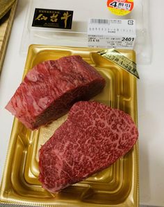 two pieces of raw meat sitting on top of a gold tray next to a measuring tape