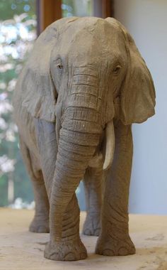 an elephant made out of clay standing on a wooden table in front of a window