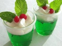 two cups filled with green drinks and topped with whipped cream, cherries and mint leaves