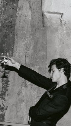 a woman holding a wine glass in her right hand and pointing at something on the wall