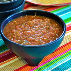 there is a bowl of salsa on the table with tortillas in the background