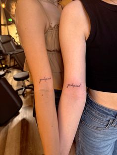 two women with matching tattoos on their arms, one is holding the other's arm