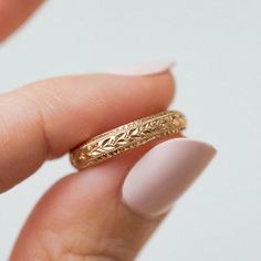 a woman's hand holding a gold ring with an intricate design on the side