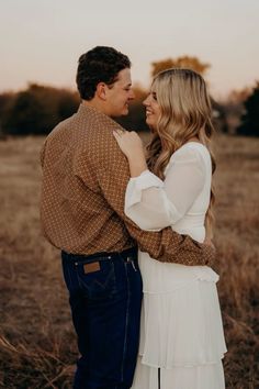 a man and woman are standing together in the middle of an open field at sunset