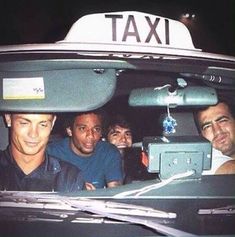 four men are sitting in the back of a taxi cab, looking at the camera