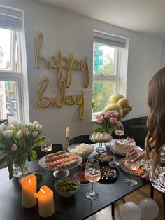 a woman standing in front of a table filled with food and drinks next to a large happy birthday sign