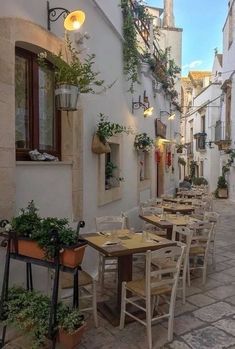 an alleyway with tables and chairs lined up along the side of it, in front of white buildings