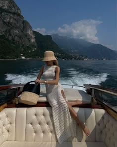 a woman sitting on the back of a boat with a purse in her hand and mountains in the background