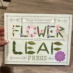 a hand holding up a flower and leaf press card with flowers on it's side