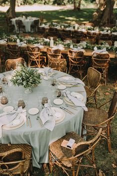 a table set up with plates and place settings for an outdoor wedding reception in the woods