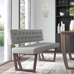 a gray bench sitting on top of a rug next to a wooden table and bookcase