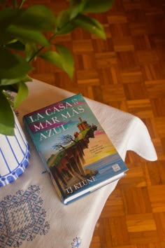 a book sitting on top of a table next to a vase filled with green plants