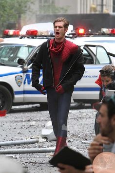 a man in a red and black spider suit is on the street with police cars behind him