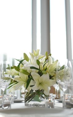 a vase filled with white flowers sitting on top of a table next to wine glasses