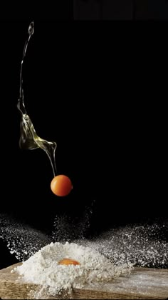 an orange being thrown into the air by water on top of a cutting board with flour