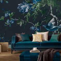 a blue couch sitting in front of a wall with flowers and birds painted on it