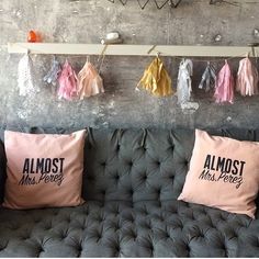 three pink and gold pillows hanging on a gray wall next to a grey couch with black letters that read almost most people