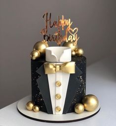 a black and white birthday cake with gold decorations on it's top, topped with a bow tie