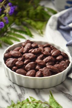 a white bowl filled with chocolate chips on top of a marble counter next to purple flowers