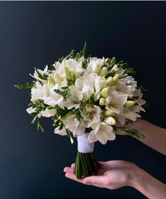 a bouquet of white flowers being held by someone's hand in front of a dark background