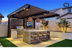 an outdoor kitchen and bar area with lights on the roof, surrounded by artificial grass