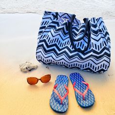 a pair of flip flops, sunglasses and tote bag sitting on the beach