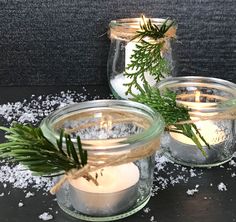 three jars filled with candles sitting on top of a table covered in snow and pine needles