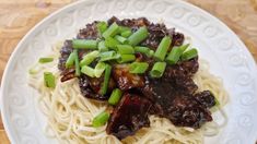 a white plate topped with pasta and meat covered in sauce, green onions and scallions