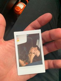 a hand holding a polaroid with a woman talking on a cell phone in the background