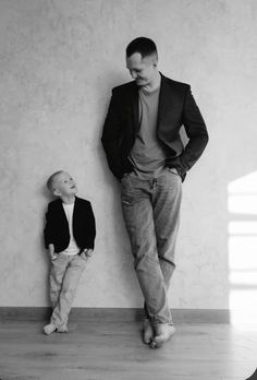 a man standing next to a little boy in front of a wall with his hands on his hips