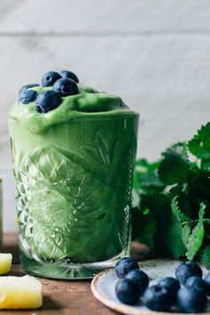 a green smoothie with blueberries and lemon slices on the side next to it