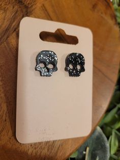 pair of black and white skull studs on wooden table next to green plant area