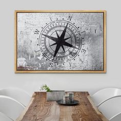 a wooden table topped with white chairs next to a wall mounted art print on the wall