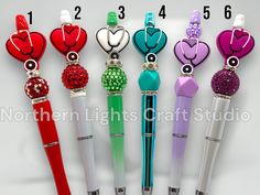 four different colored pens with hearts and beads on them, all lined up in a row