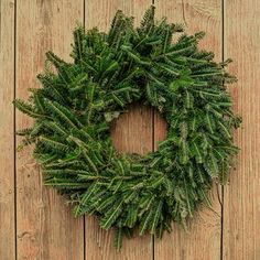 a wreath is hanging on the side of a wooden fence, with pine needles in it