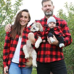 a man, woman and baby are standing in an apple orchard with their dog on his lap