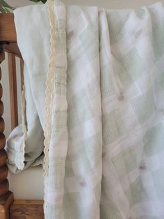 a white and green blanket sitting on top of a wooden chair next to a plant