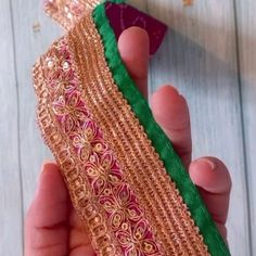 a person is holding a piece of cloth with gold thread and green material on it