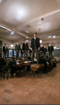 a group of young men standing on top of desks in a room with wooden floors